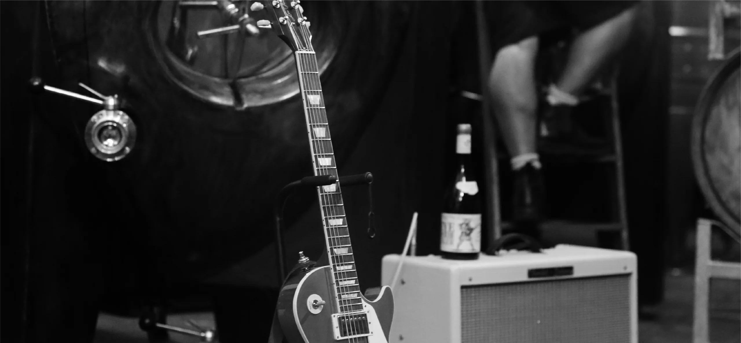 Guitar and amplifier in foreground with wine vat blurred in background – Orpheus and the Raven logo image
